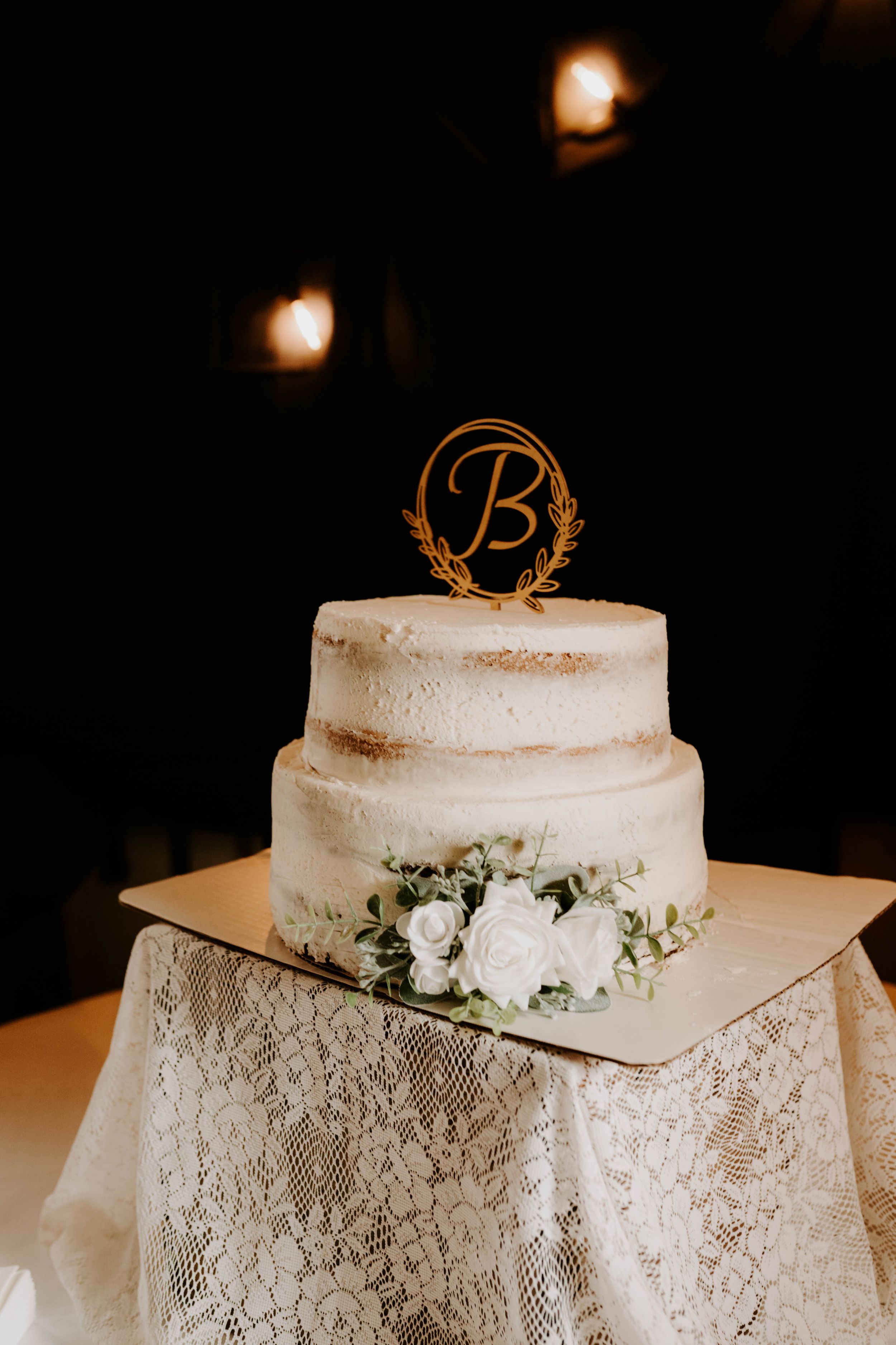 Elegant white wedding cake with lace tablecloth and monogram topper.