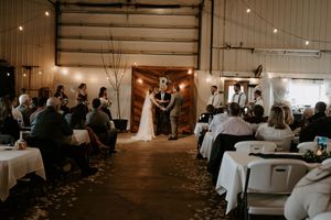 Wedding reception venue with string lights and guest seating in a rustic indoor space.