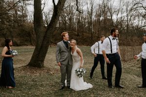 Bridal party in navy dresses and groomsmen in suspenders pose in winter woods.