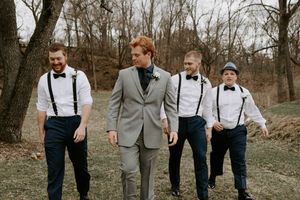 Wedding party members in suits and suspenders walk together on a grassy hill during autumn.
