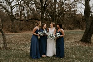 Wedding party members in navy dresses and white gown gather for photos in a natural outdoor setting.