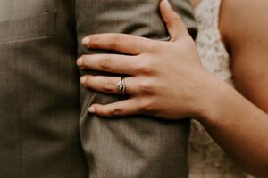 Close-up shot of hands displaying wedding rings against grey fabric.