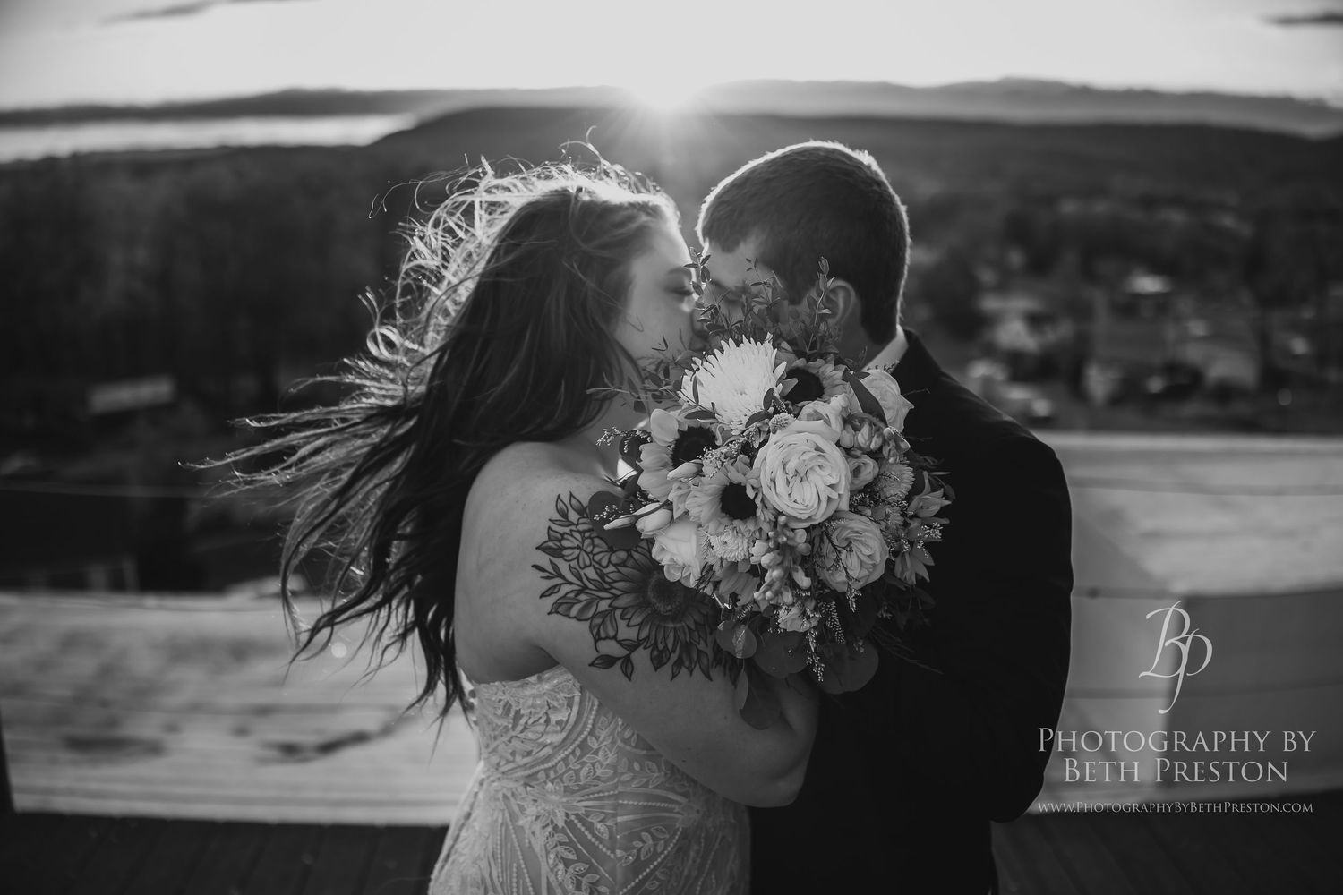 A couple shares a romantic moment outdoors with a bridal bouquet of white flowers as the wind blows through her hair.