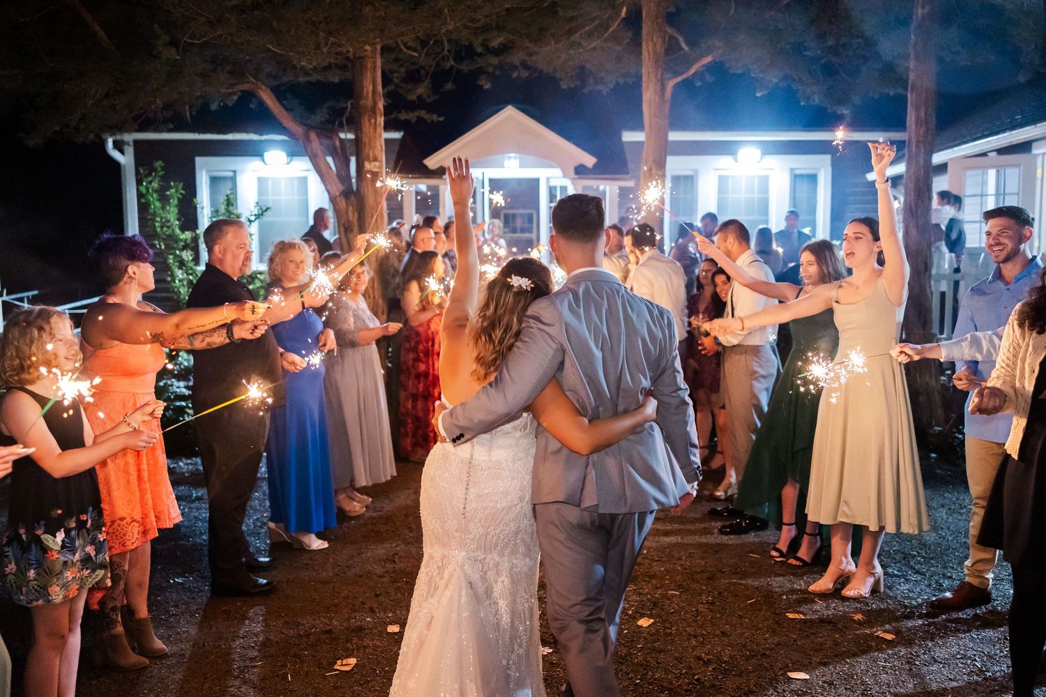 Wedding guests dance together at an evening outdoor reception under string lights and a covered pavilion.