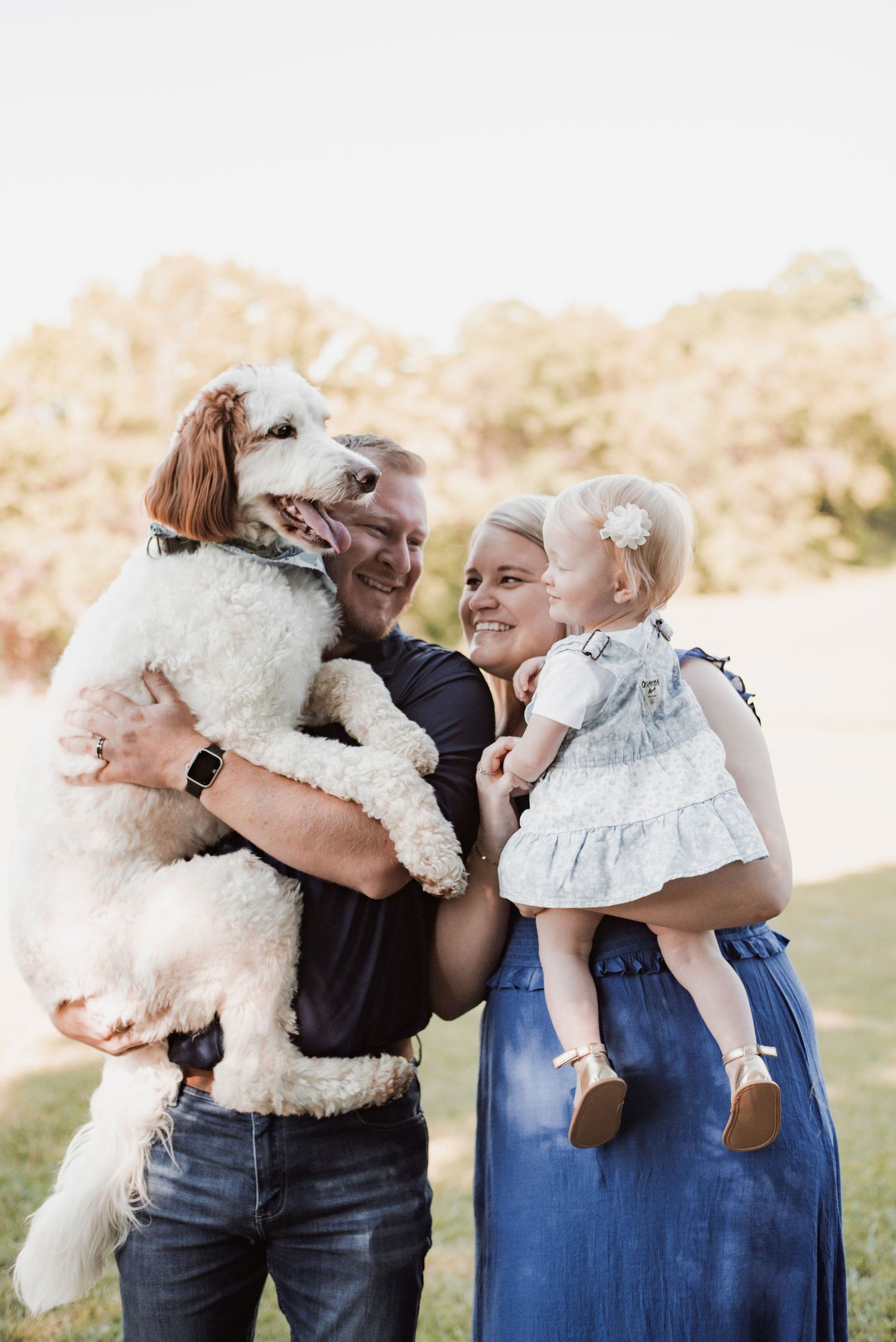 A family of 3 posing with their dog for family photos at home.