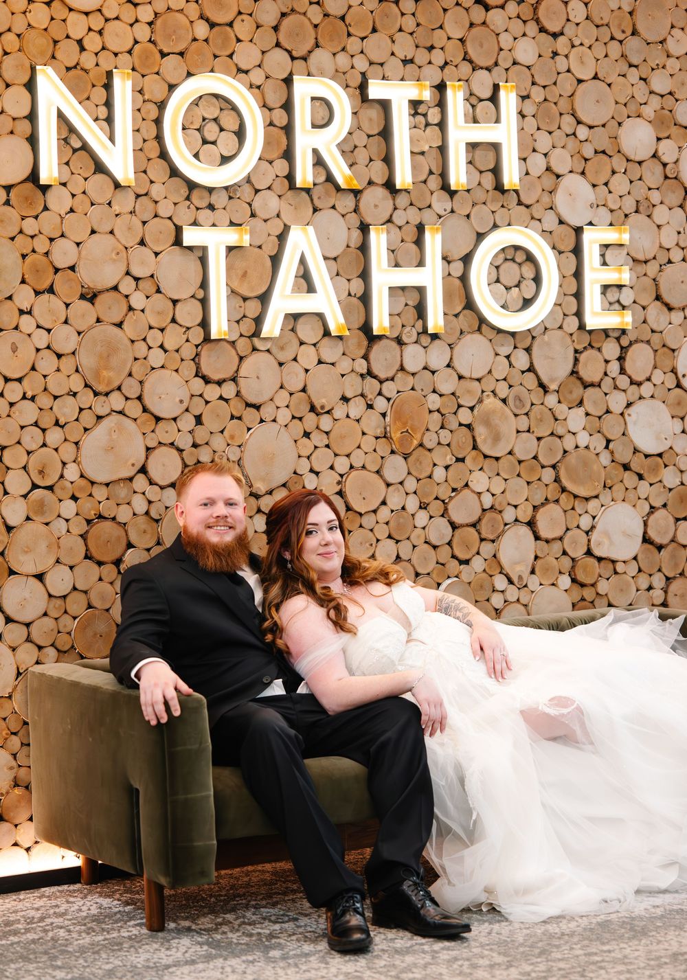 Wedding couple sitting together against rustic wooden wall display with 'NORTH TAHOE' text at mountain resort venue.