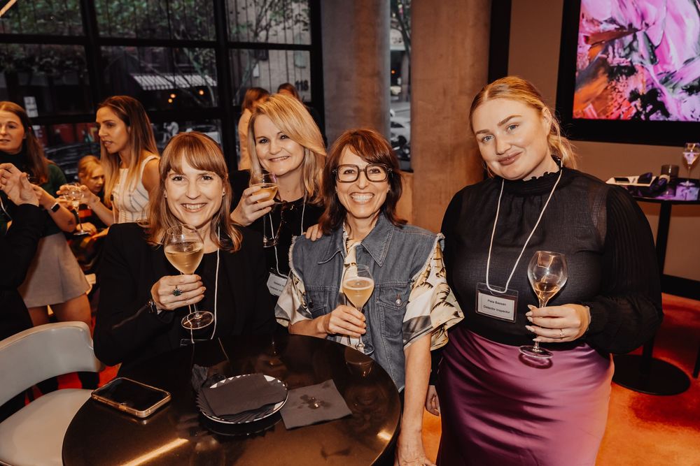 A group of women smile while enjoying drinks together at a dimly lit bar or restaurant.