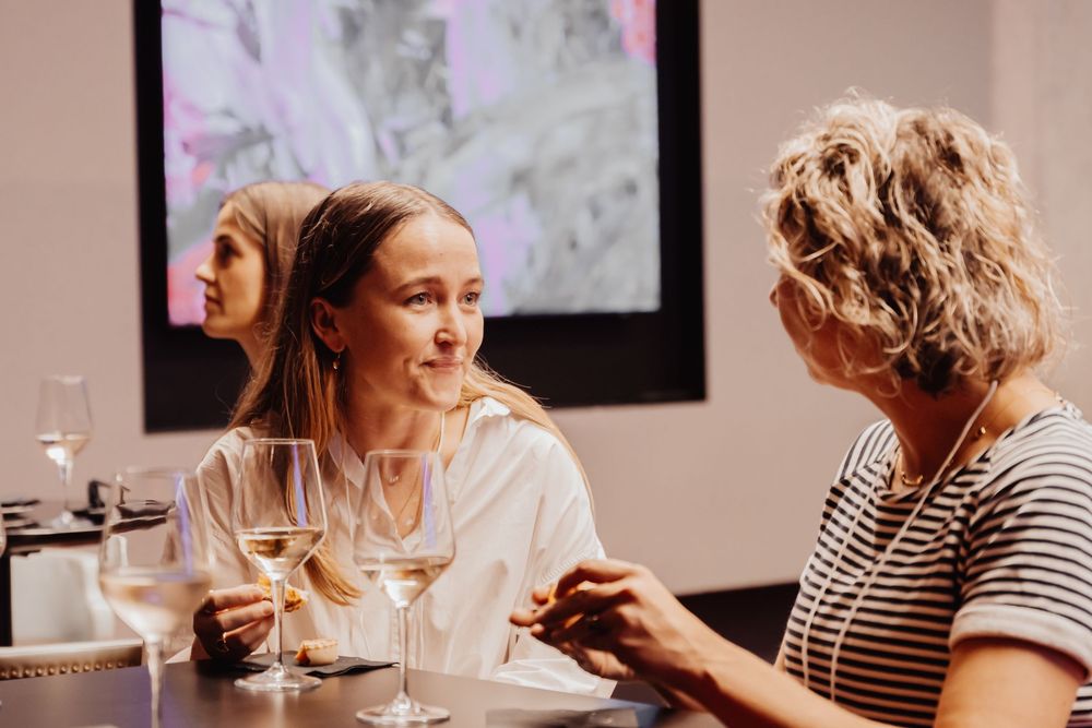 People enjoying wine tasting and conversation in an elegant indoor setting with glassware on table.