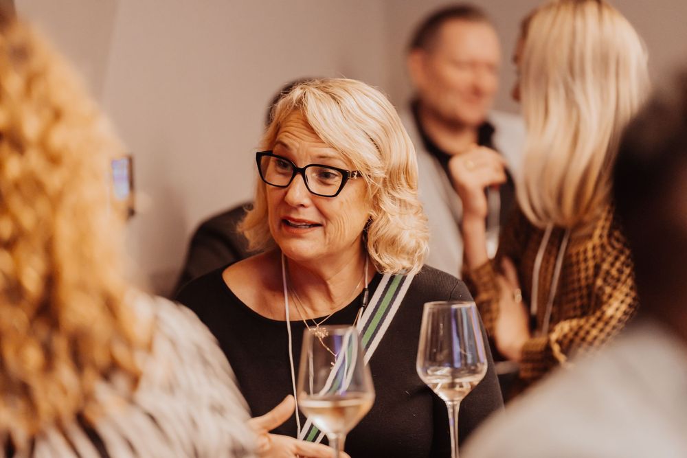 People enjoying wine and conversation at an upscale social gathering with warm lighting and wine glasses.