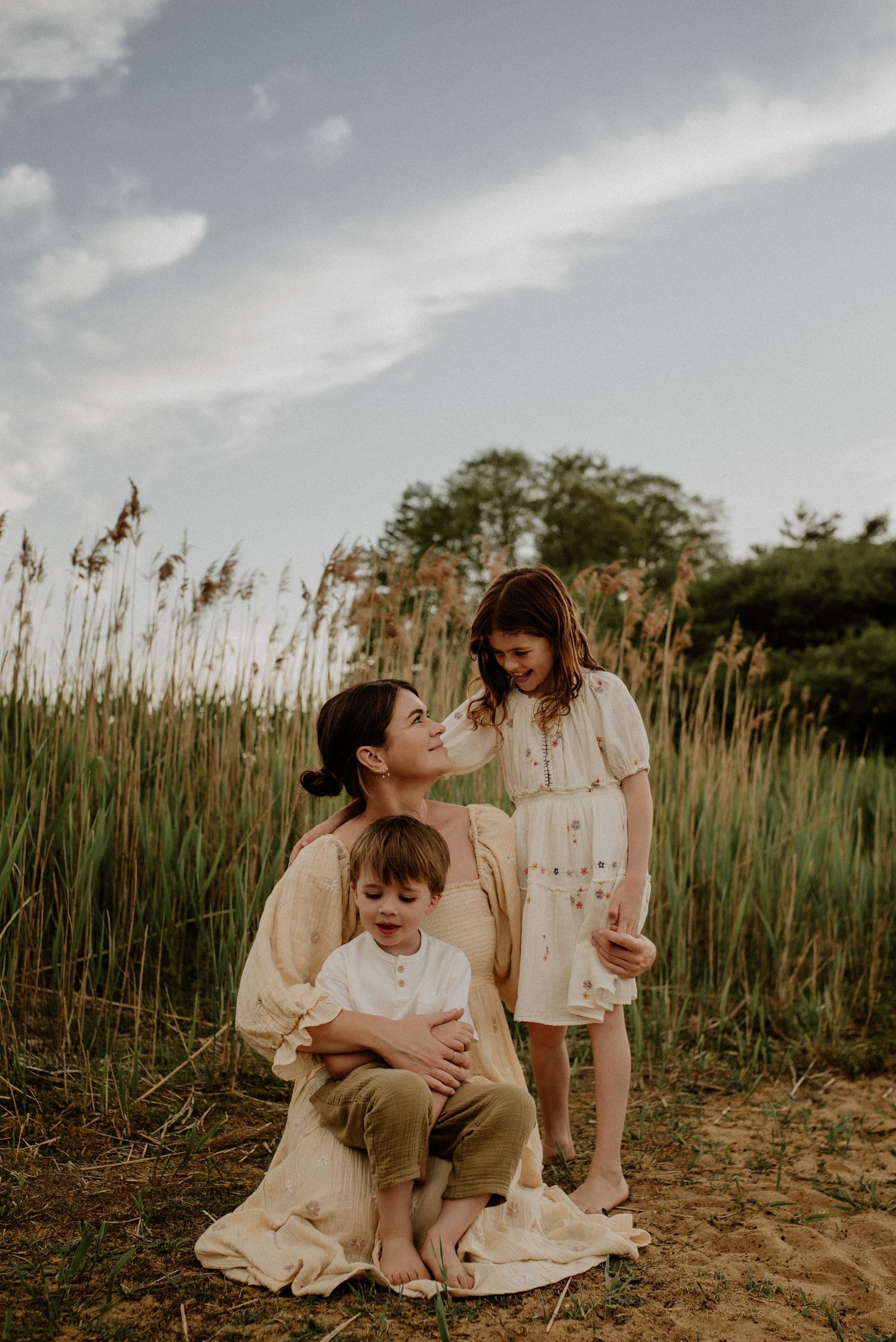 A tender family moment captured in a field of tall reeds during golden hour with soft sunlight and dreamy atmosphere.