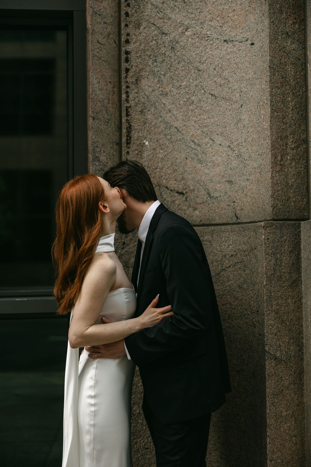 Intimate moment between couple in formal wear against stone wall.