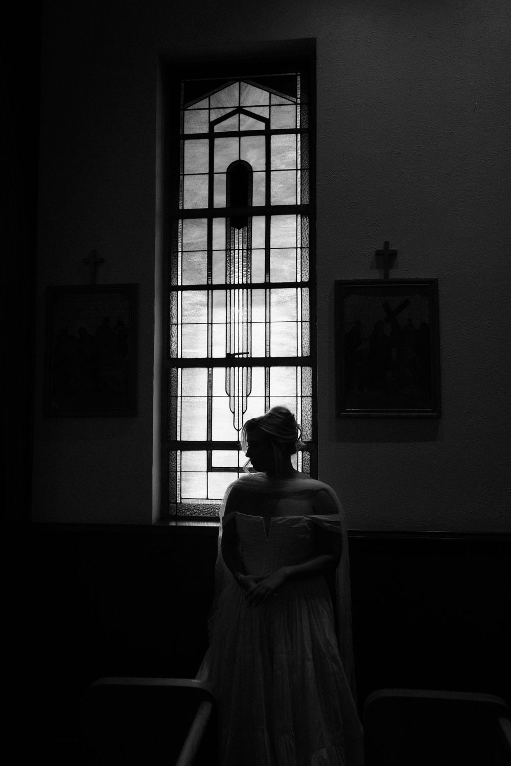 A silhouetted figure stands in front of a bright church window creating a dramatic contrast in black and white.