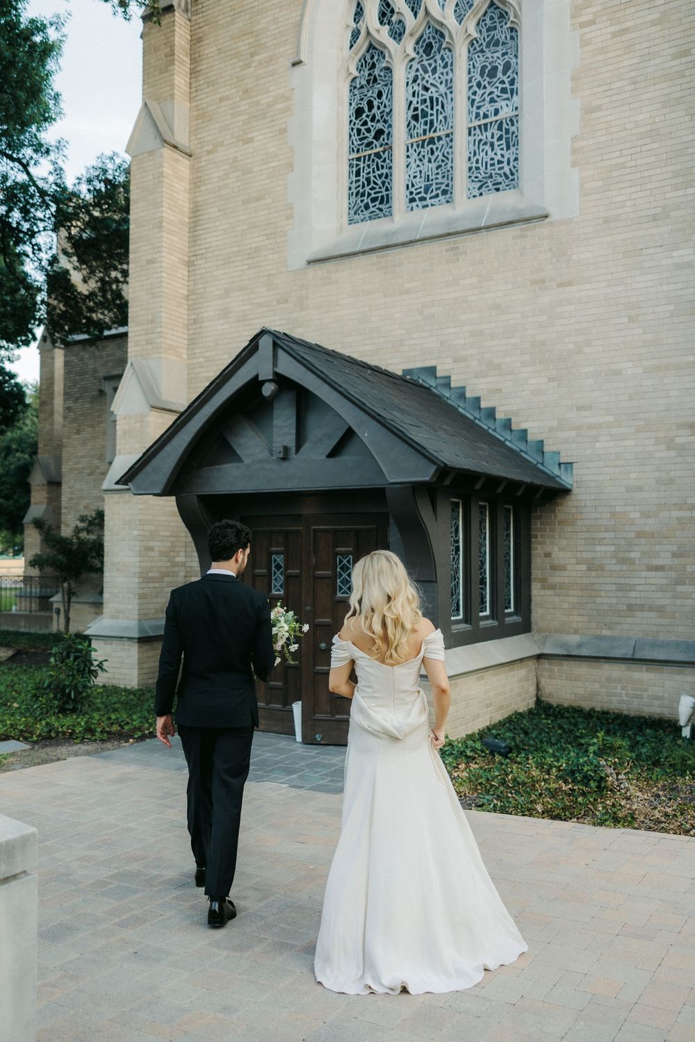 Wedding couple walking towards church entrance with gothic windows.