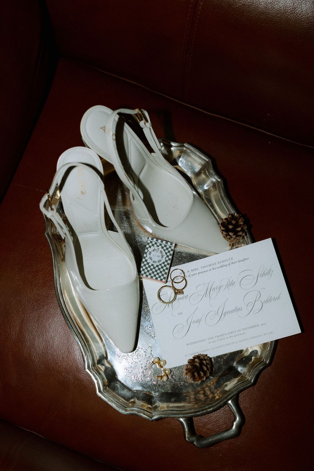 A white paper invitation card with elegant script text rests on a decorative silver or mirrored tray in low light.