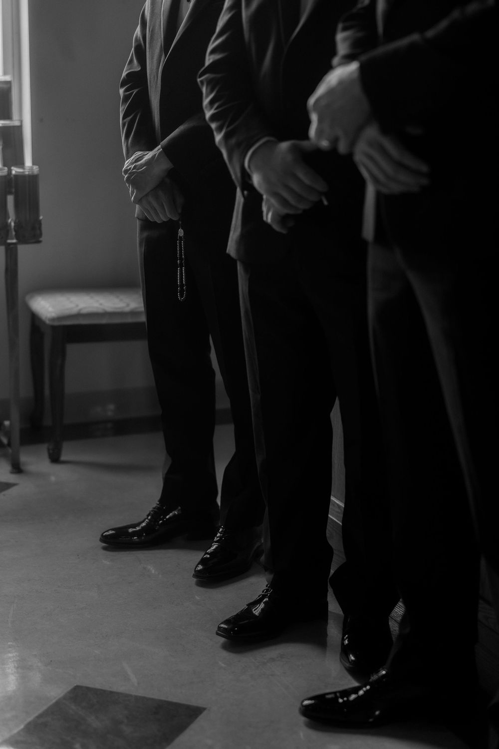 Black and white detail shot of groomsmen's polished dress shoes and suit pants.