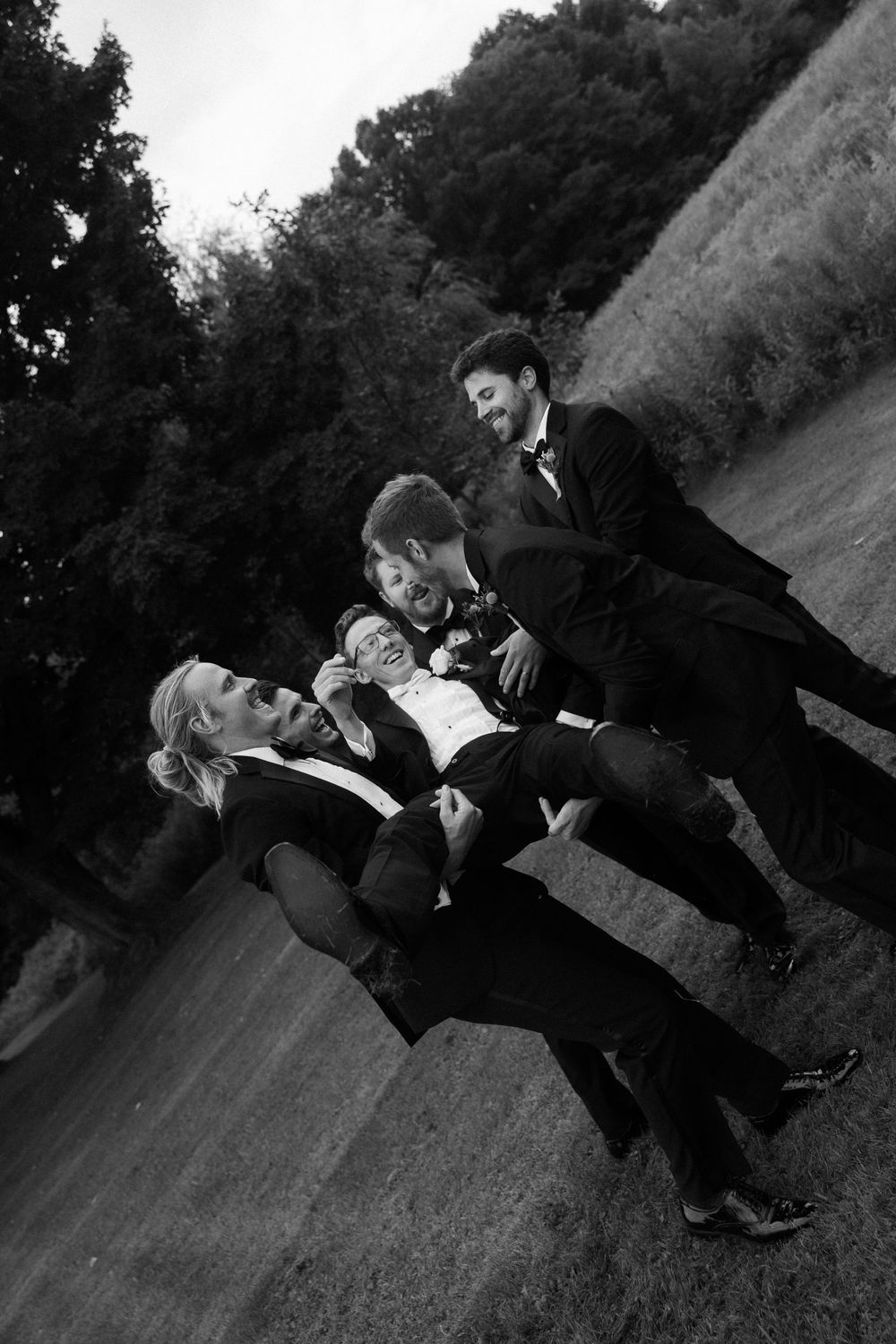 A series of black and white photos showing a couple in formal attire playfully falling over in sequence.