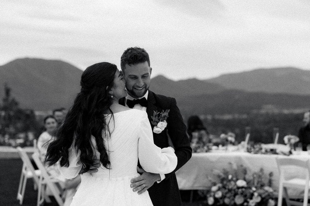 A couple embraces during their wedding ceremony with mountains and a scenic landscape in the background.