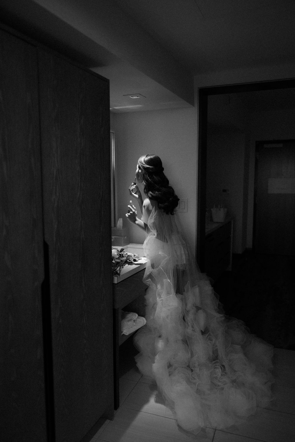 A bride in a flowing white wedding gown walks through a dimly lit hallway creating a dramatic silhouette effect.