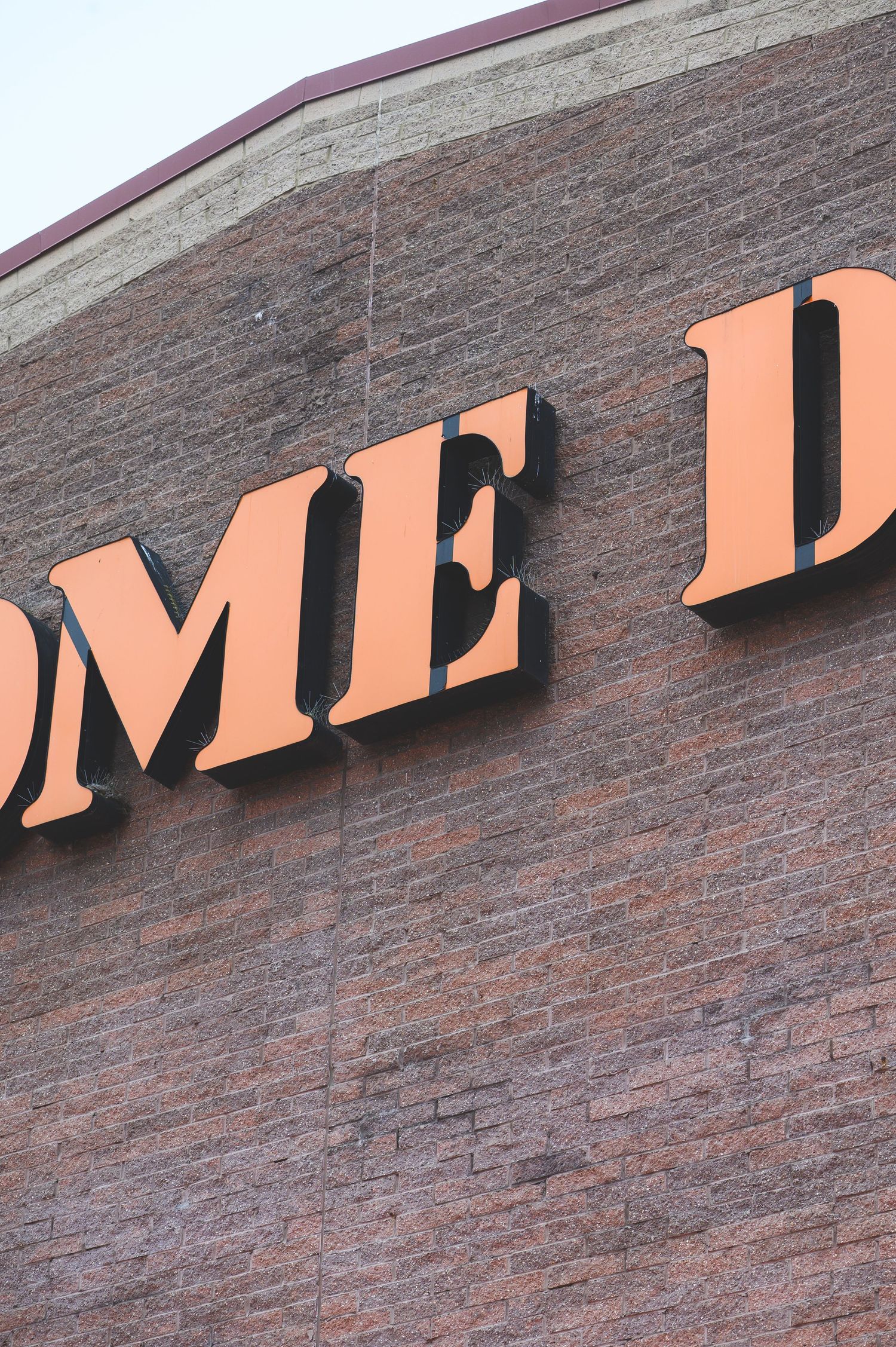 Large orange letters mounted on a brown brick wall showing partial text reading 'OME D'.