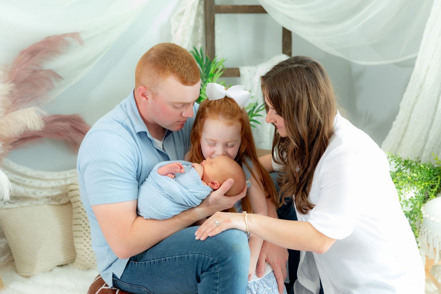 A family shares a tender moment together while sitting on white cushions with sheer curtains in the background.