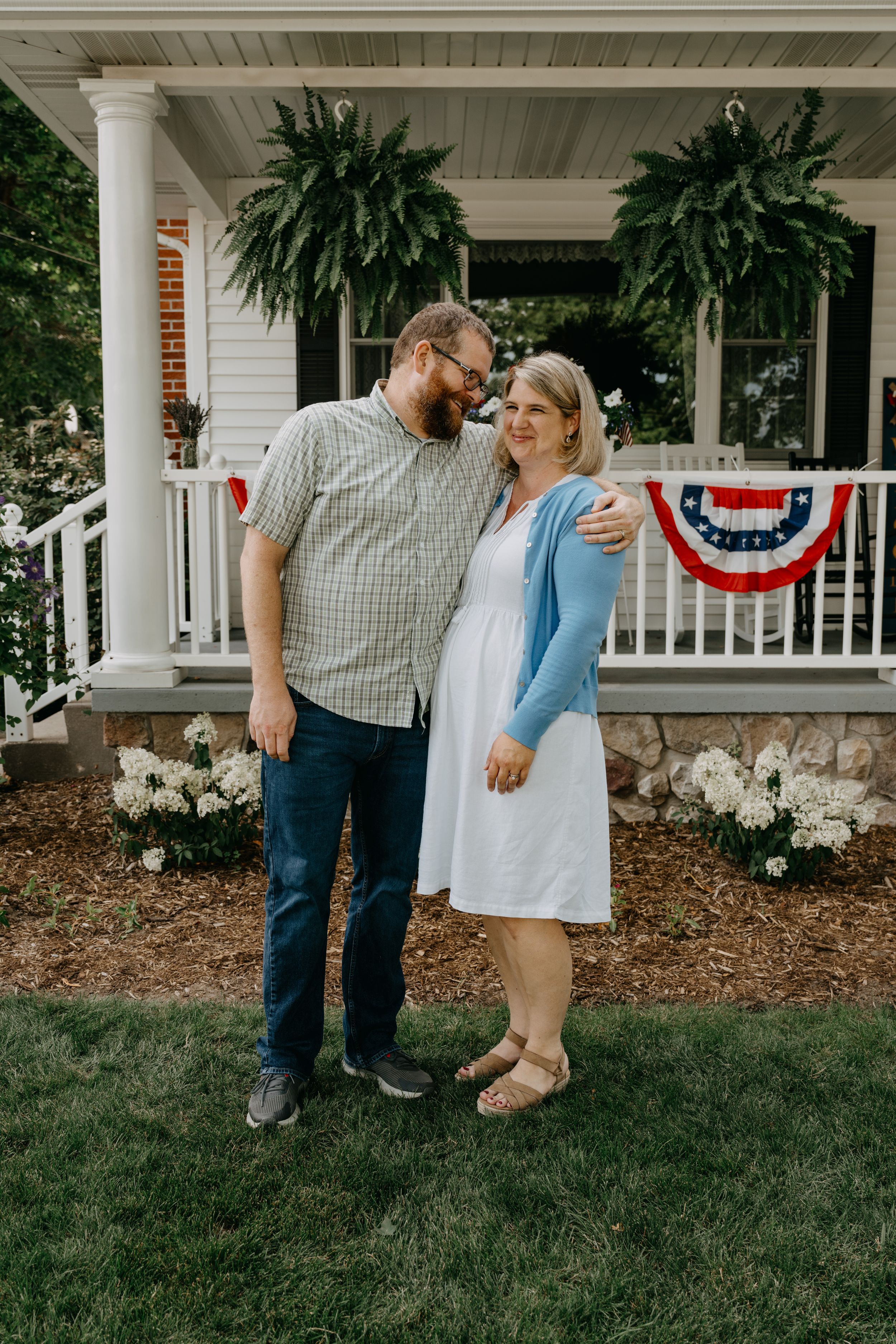 A couple shares a sweet moment on their porch decorated with American flag bunting and hanging ferns.