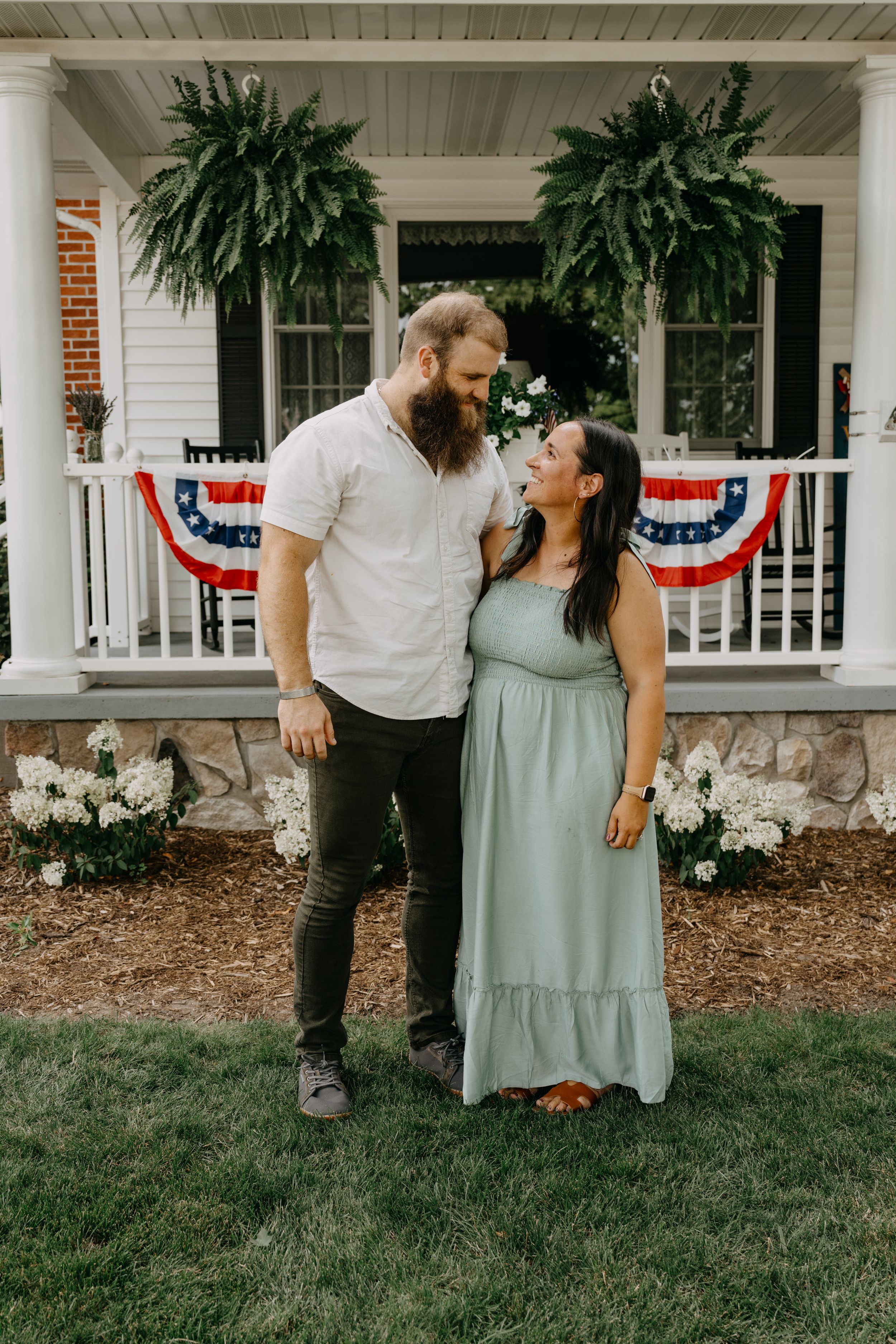 Couple standing on porch with American bunting decorations and hanging ferns in romantic patriotic summer setting.