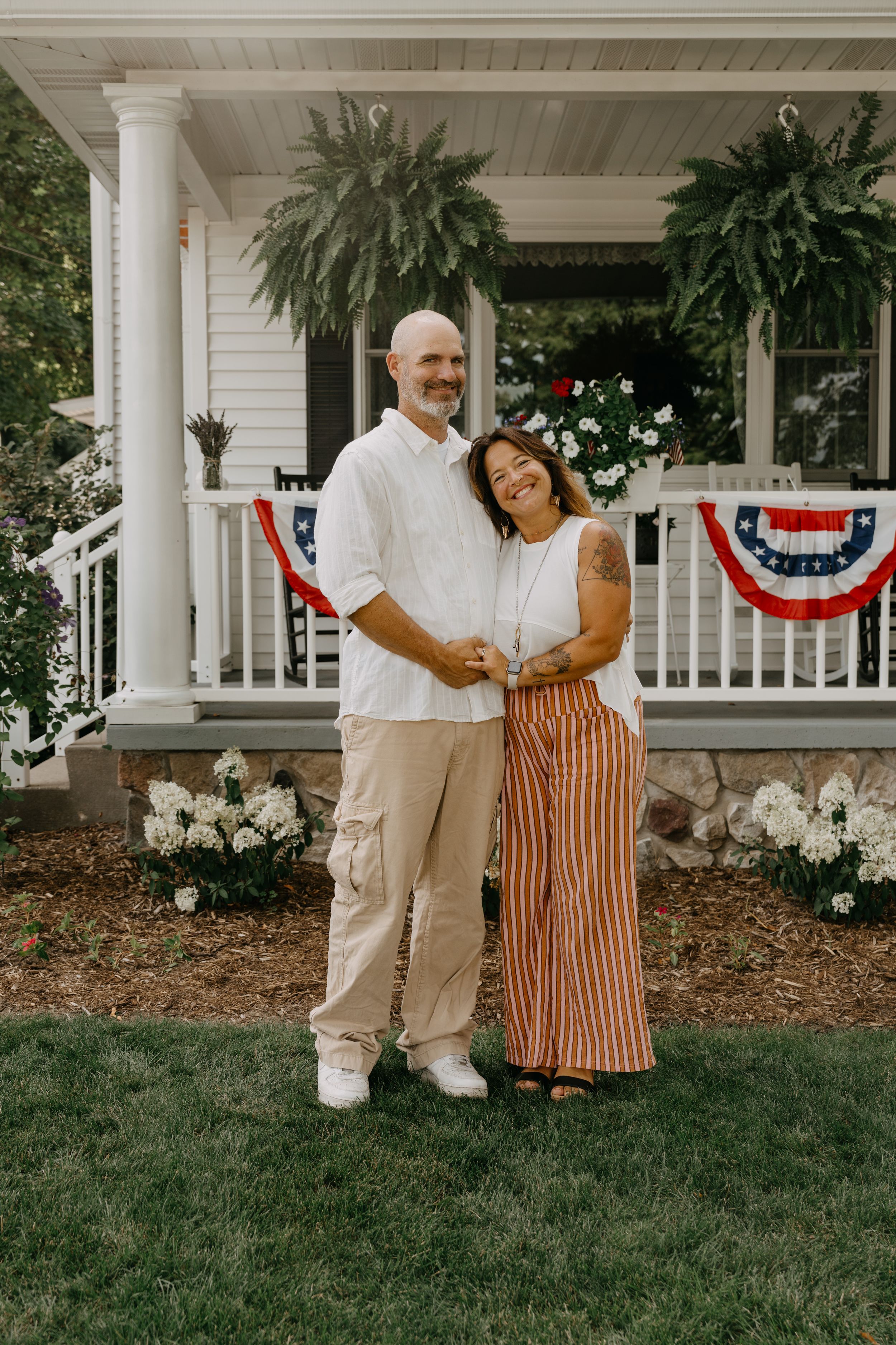 Couple enjoys time together on the porch of a white house decorated with patriotic bunting and greenery.