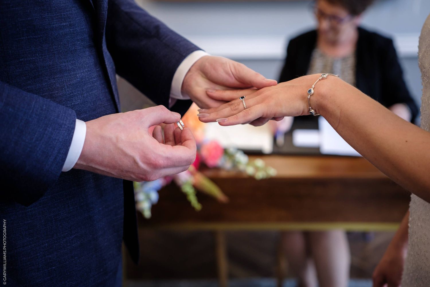 Close-up shot of a couple exchanging wedding rings during a marriage ceremony with an officiant in the background.