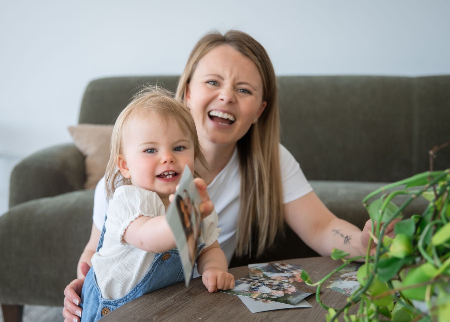 Happy parent and child share a joyful moment while looking at photos together on a gray couch.