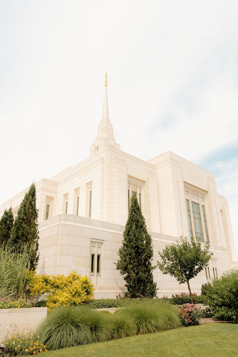 White stone temple building with spire photographed against blue sky with landscaped grounds.