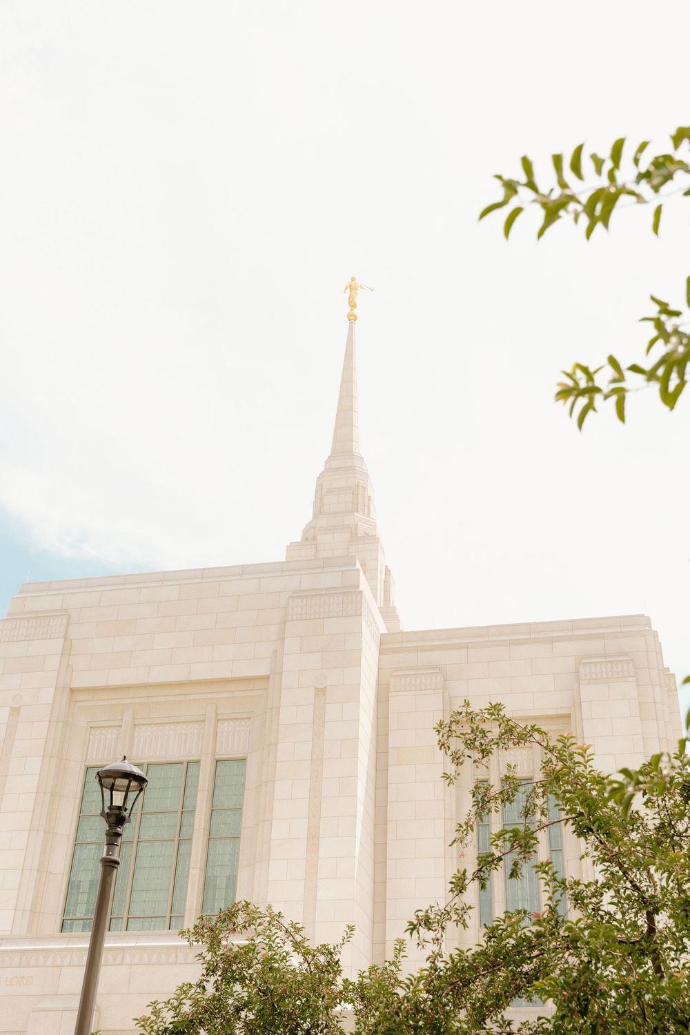White modern temple spire against blue sky with green foliage.