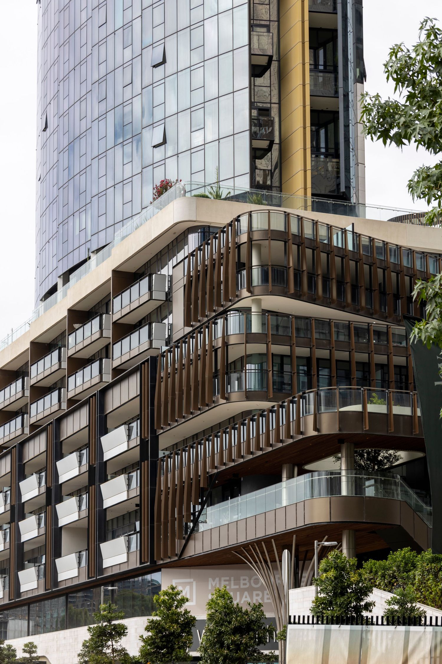 Tiered modern building with timber louvres and curved glass in late daylight.