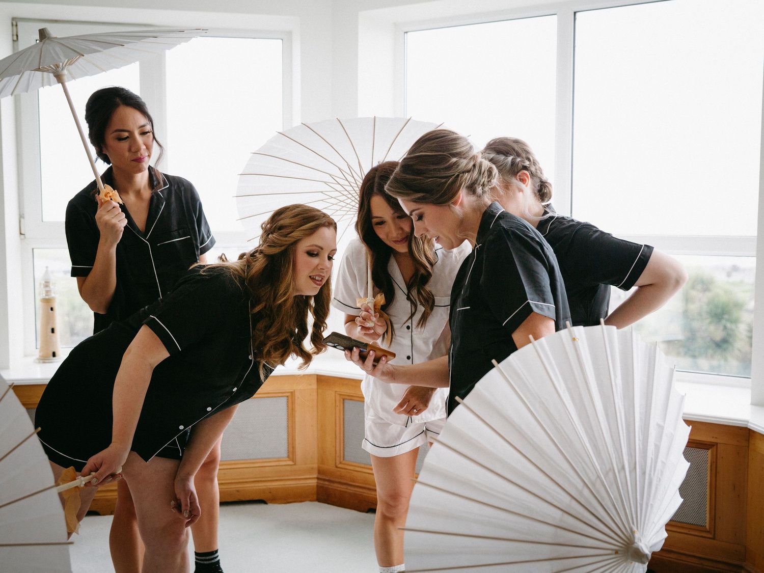 People in black and white outfits pose playfully with paper parasols in a bright windowed room.