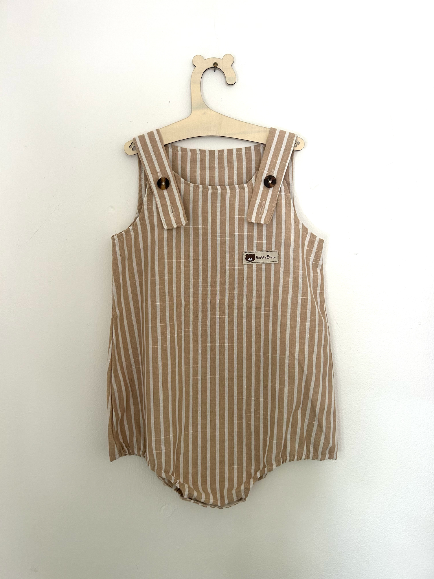 Vintage-style beige knitted baby romper with button details and side pockets hanging on display.