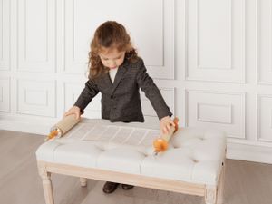 A person in business attire uses two orange toy cars to measure on a white table surface.