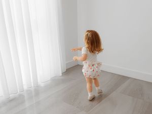 Young child in floral outfit dancing and twirling in a minimalist white room with hardwood floors.