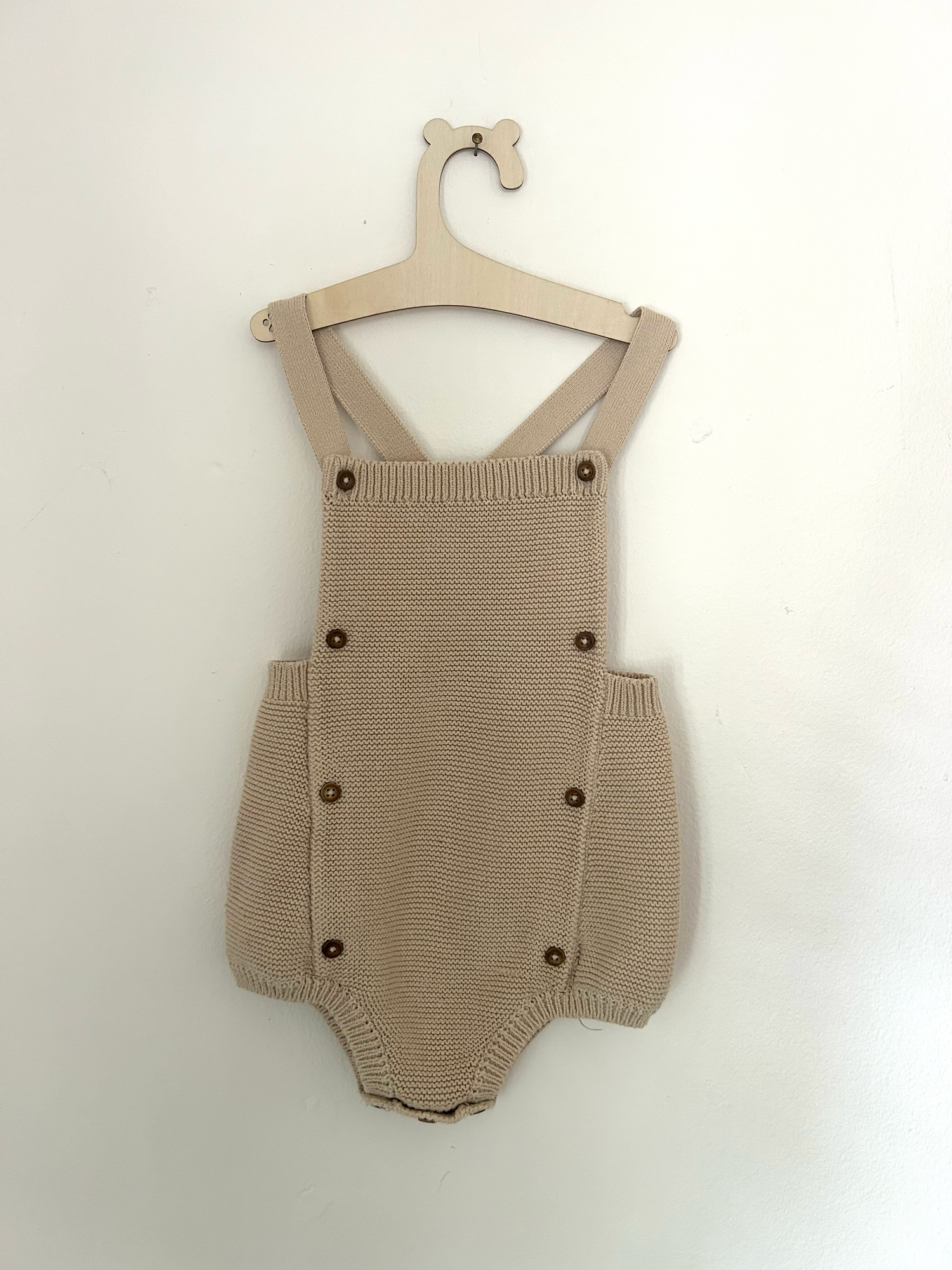 White knit baby romper with 'ONE' text and small bow detail in pink embroidery against hanging clothing background.