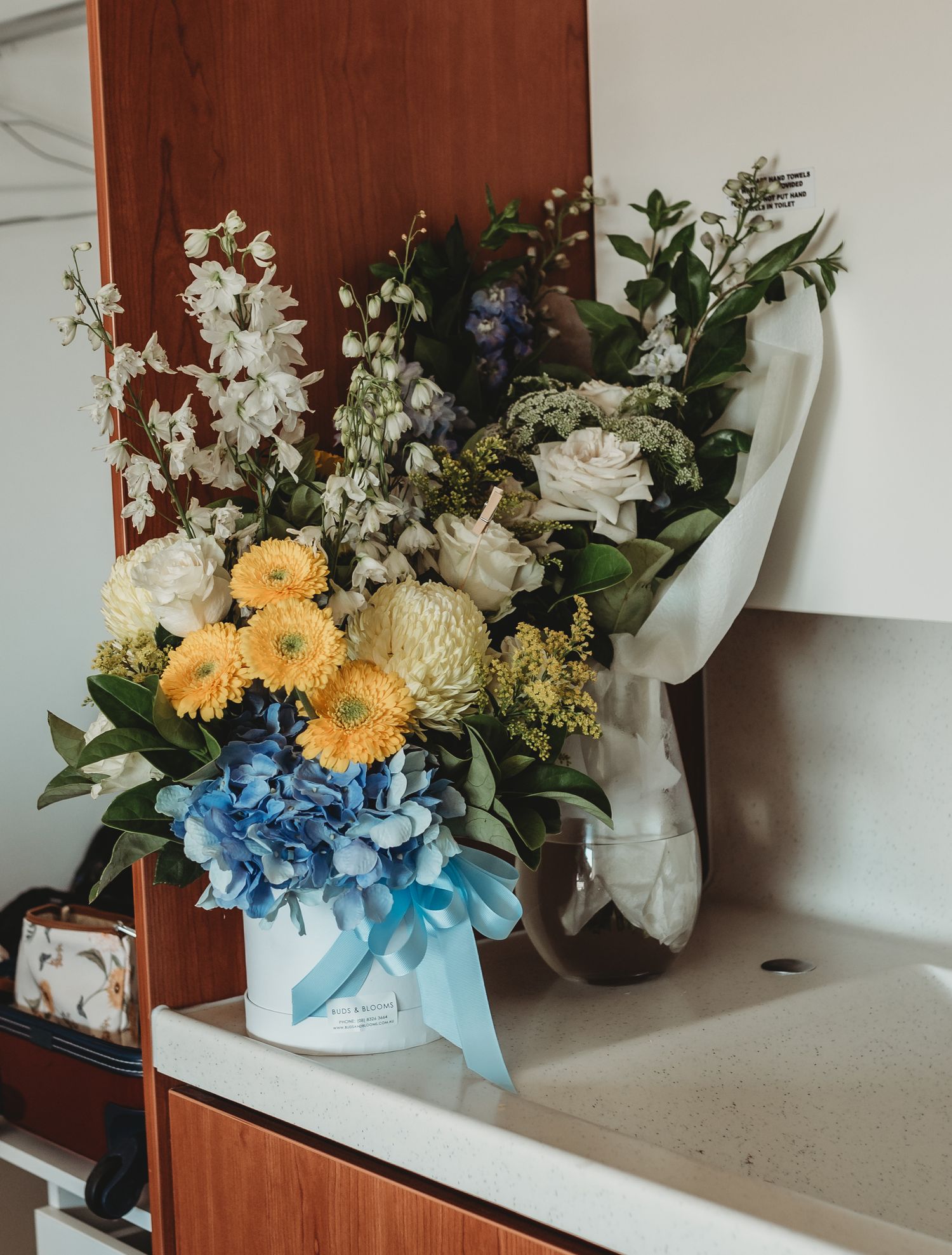 Beautiful floral arrangement with blue hydrangeas, yellow daisies, and white flowers on a counter.