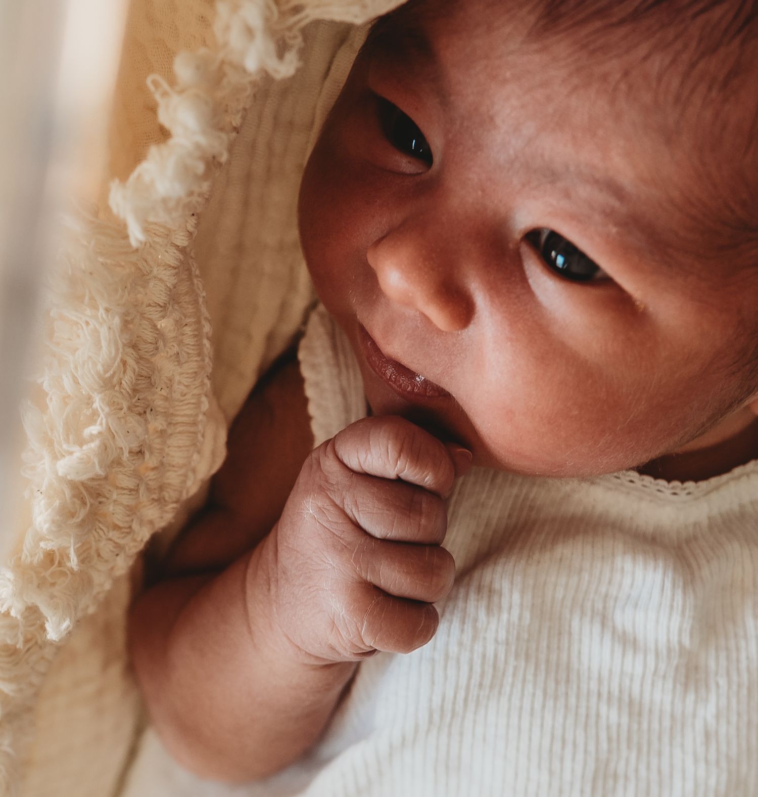 Newborn baby wrapped in delicate lace blanket smiling during a photoshoot.