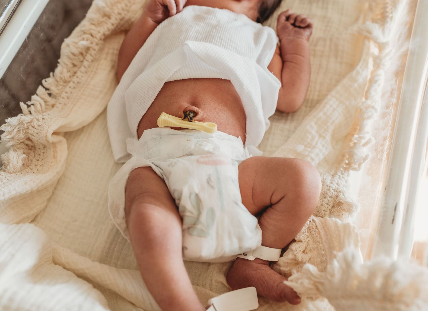 Tiny newborn baby lying in a hospital bassinet wearing white clothing.