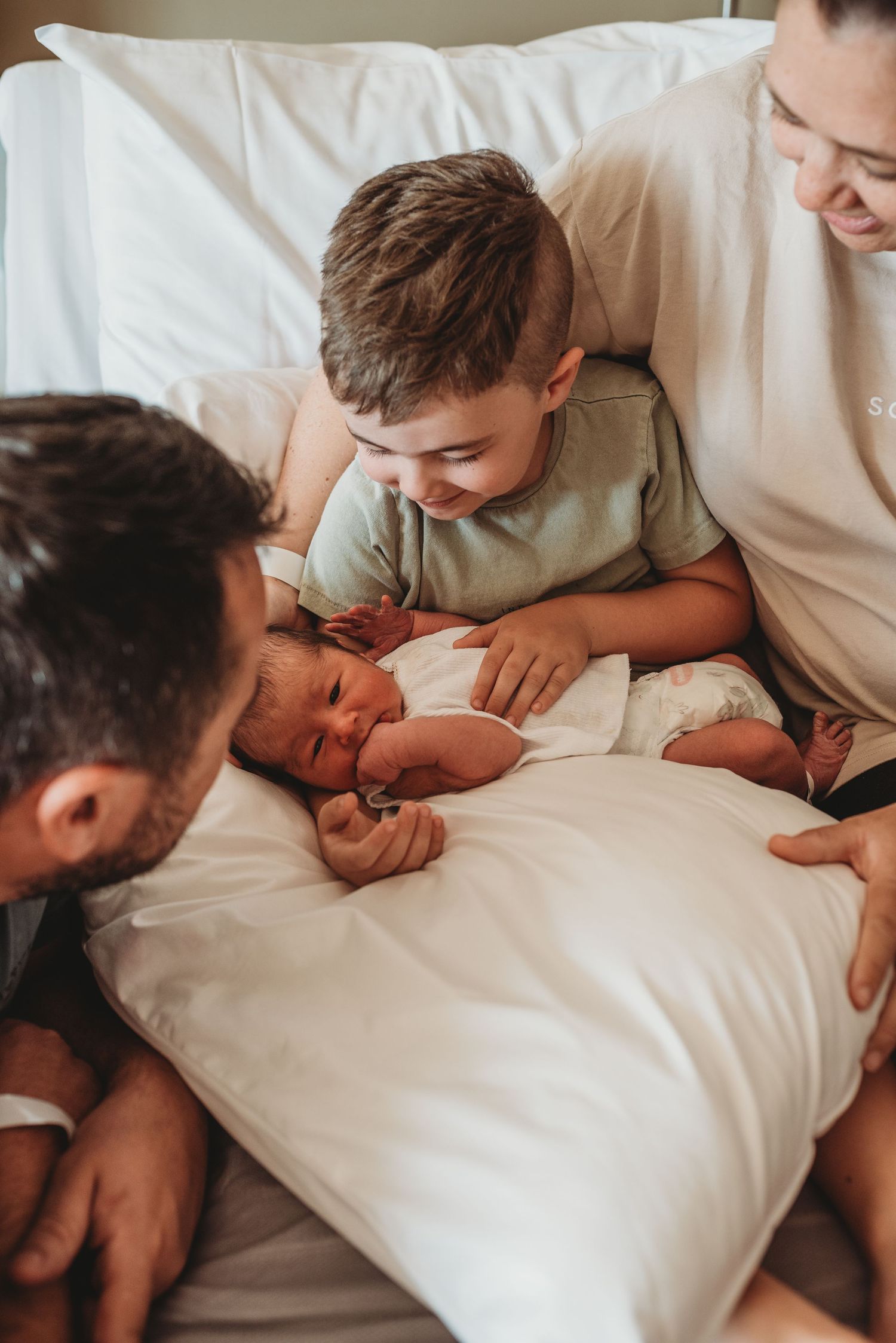 Close-up shots of family members lovingly interacting with a newborn on white bedding.