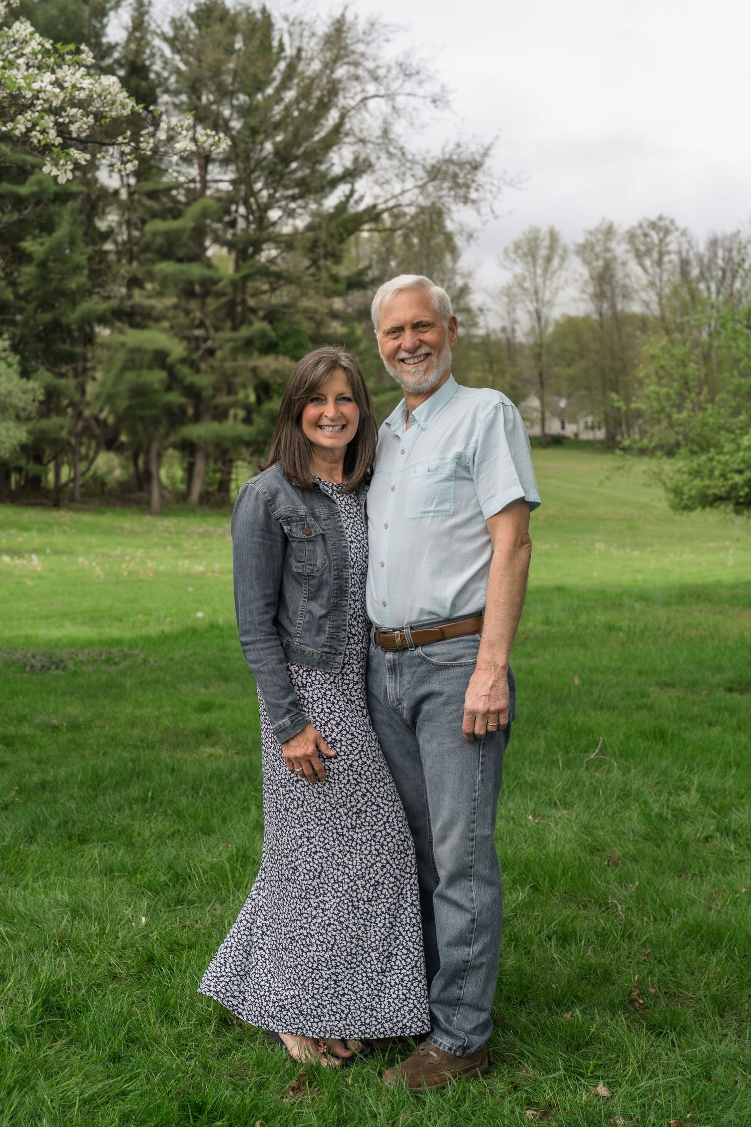 A couple stands together on a green lawn with spring trees in the background, wearing casual clothing on an overcast day in Stow, Ohio