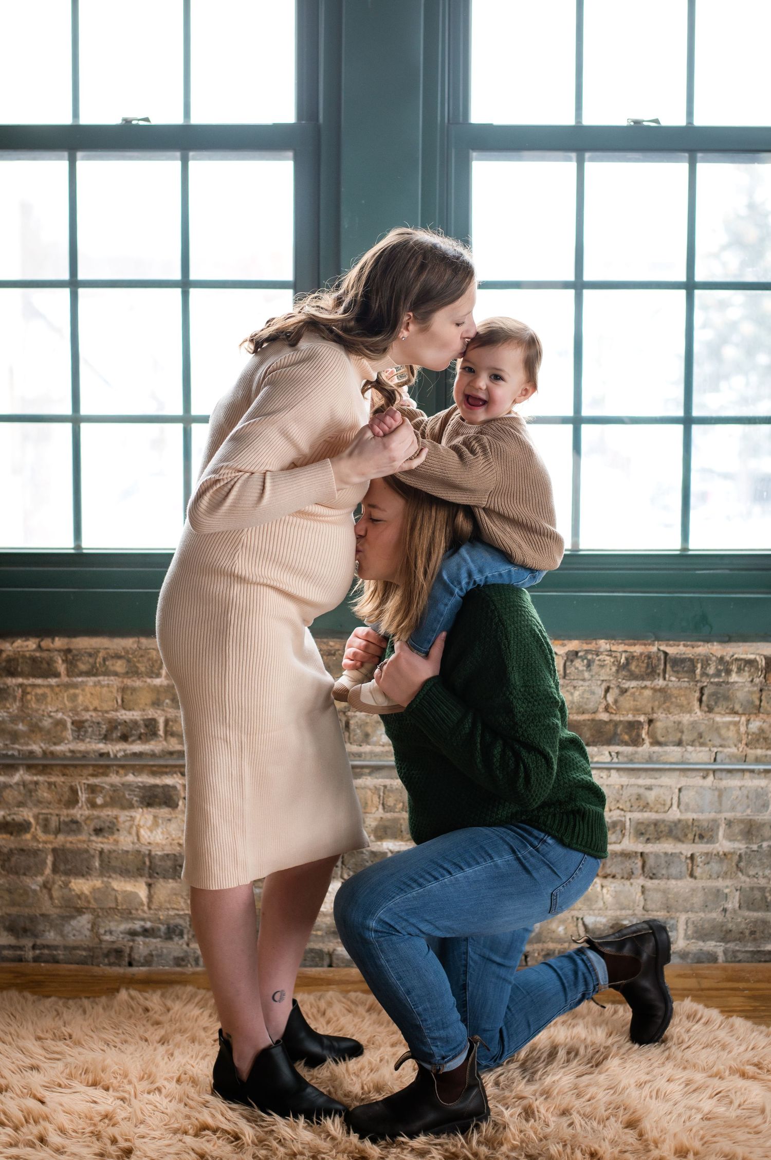Family shares tender moment together beside large windows on plush carpet in rustic brick interior space.