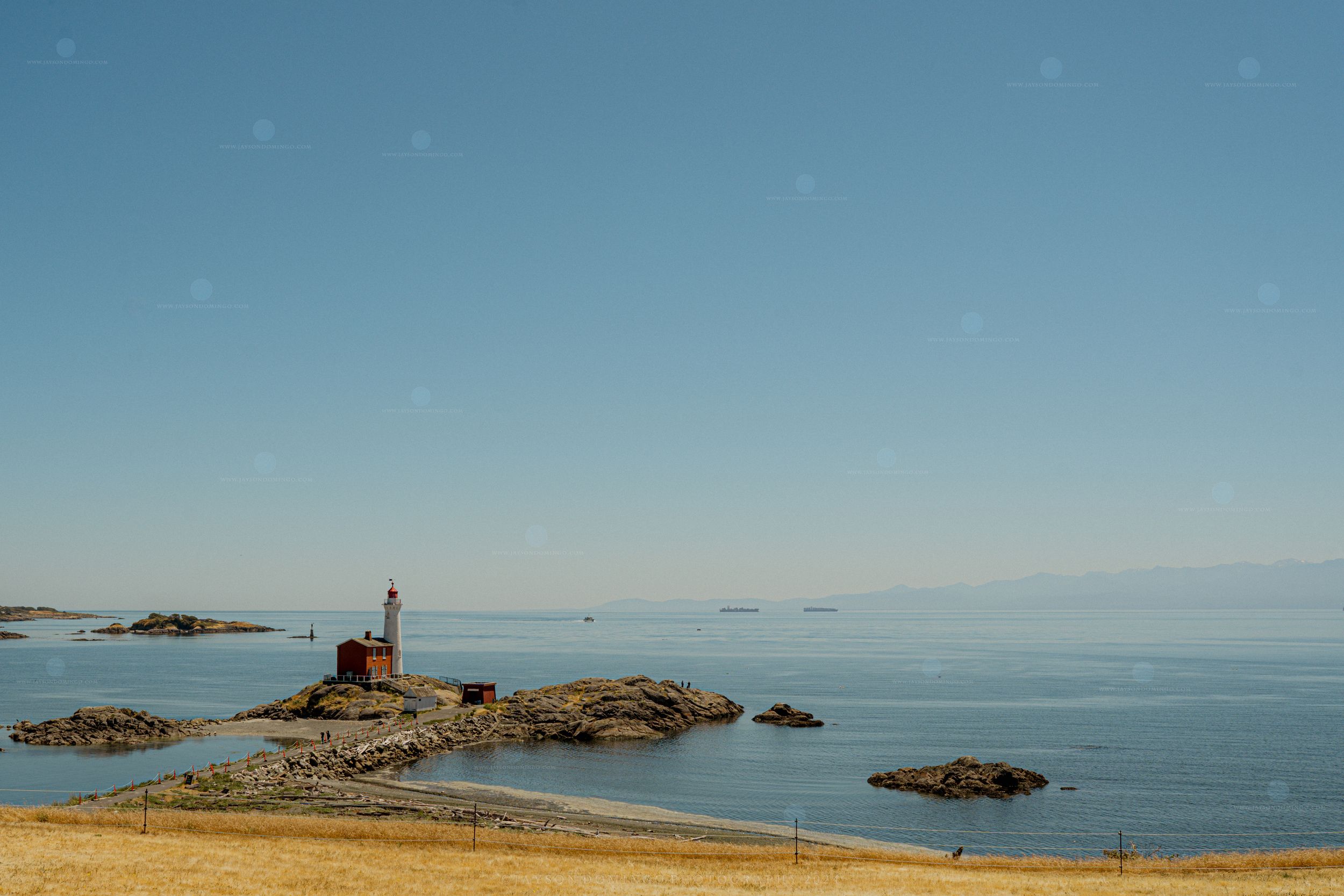 Panoramic view of rocky coastline at sunset with historic stone lighthouse perched on rugged cliffs beside calm blue sea.