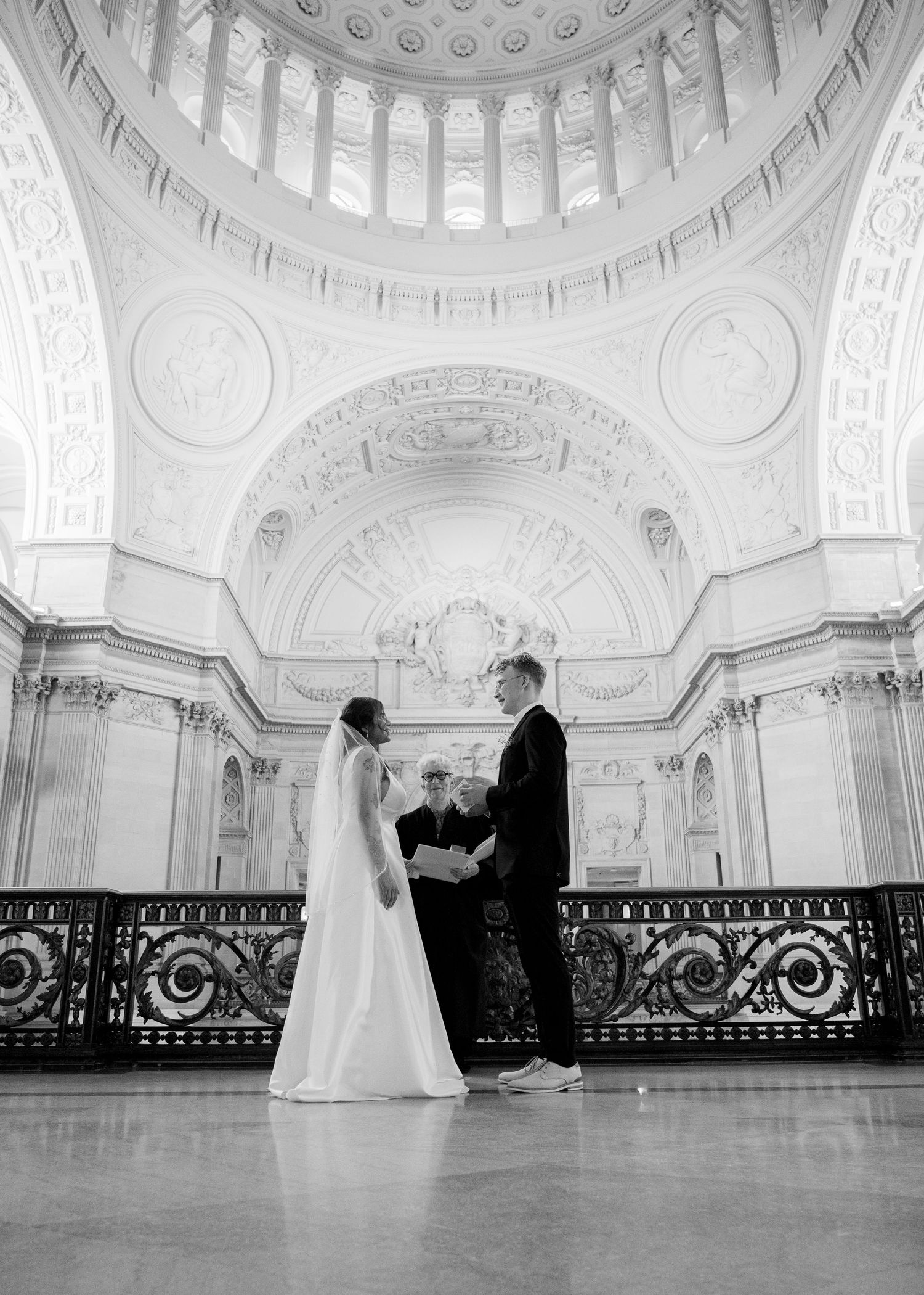 A couple sharing an intimate moment near an ornate stone column in formal wedding attire.