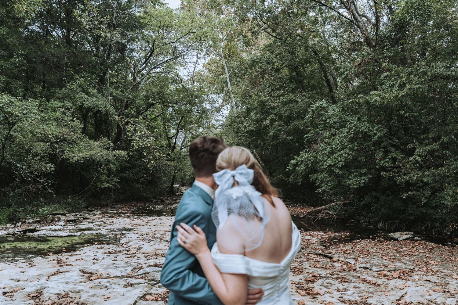 Elegant couple walks together on lush green lawn towards a rustic wooden gazebo surrounded by trees.