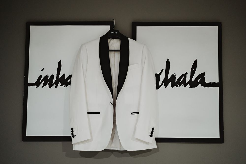 Saco del novio colgado junto a cuadros – detalle elegante de boda.