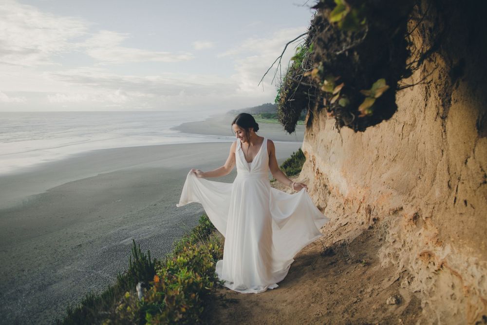 Figure in flowing white dress stands on dramatic coastal cliffside overlooking ocean vista.