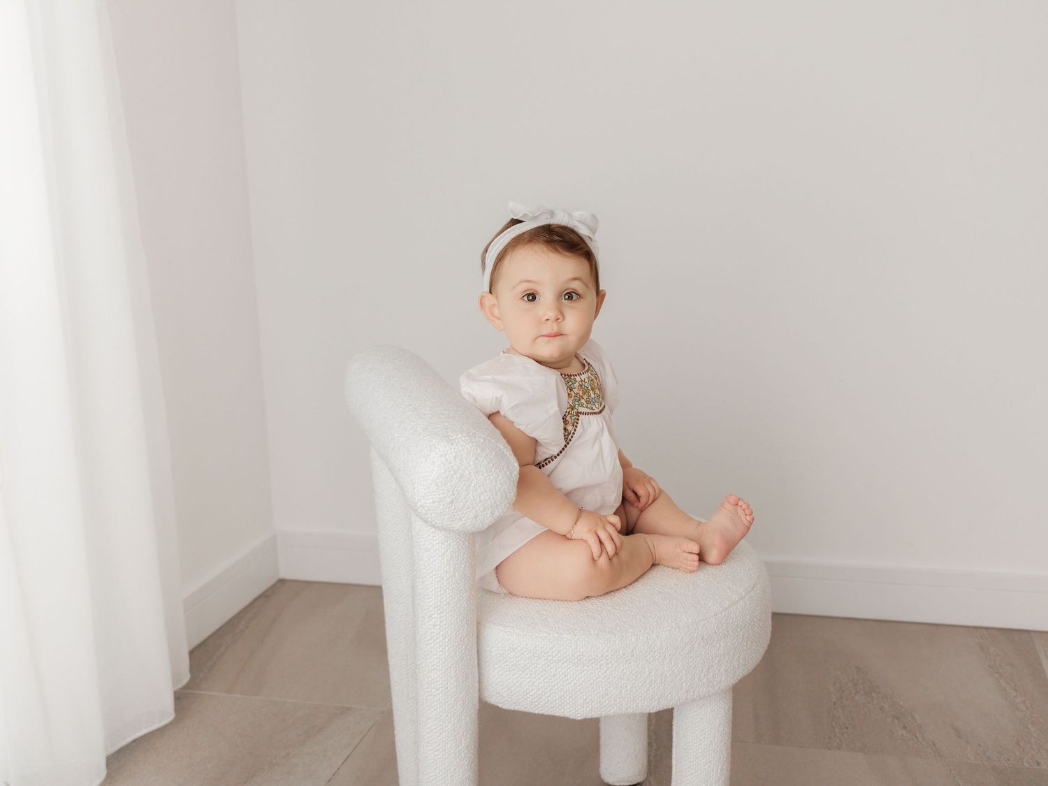 Baby seated on white cushion plays with wooden alphabet letters in bright studio setting.