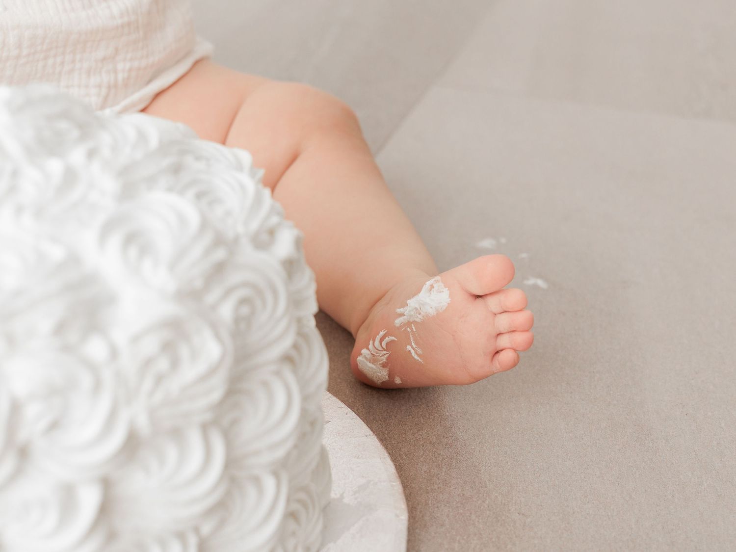 Close-up of tiny feet with lace detailing against a white dress and beige carpet.